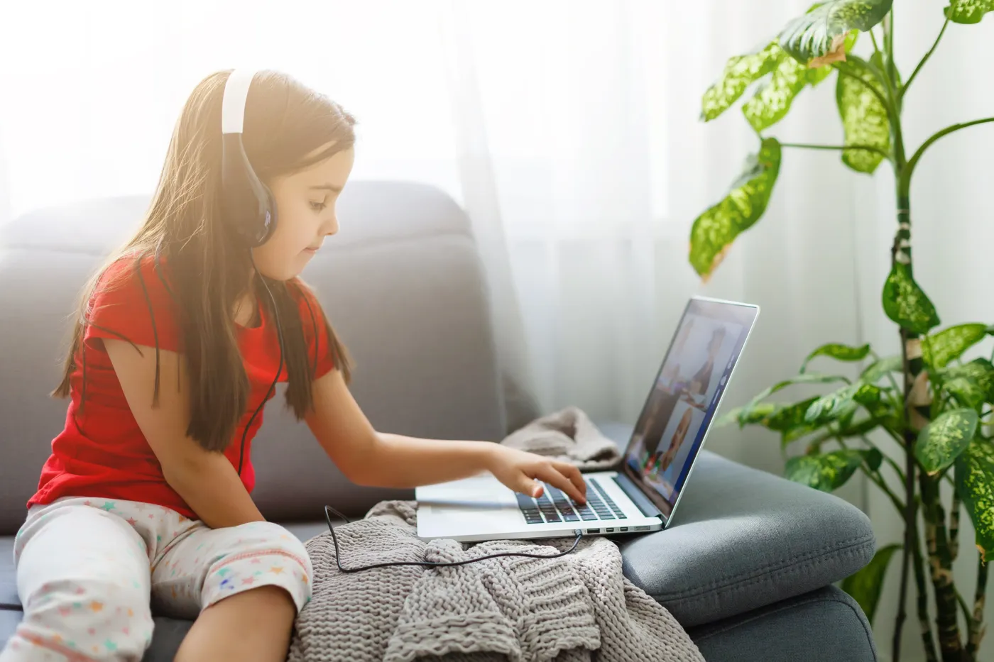 Një vajzë e vogël me kufje, duke ndjekur një mësim online në shtëpi